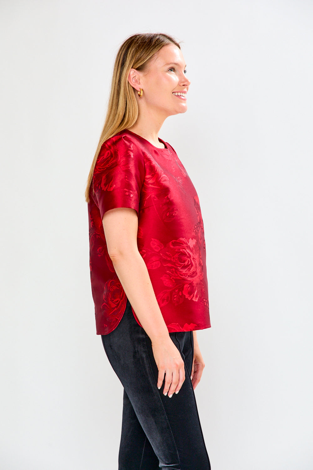 Woman wearing a red patterned top and black pants on a white background