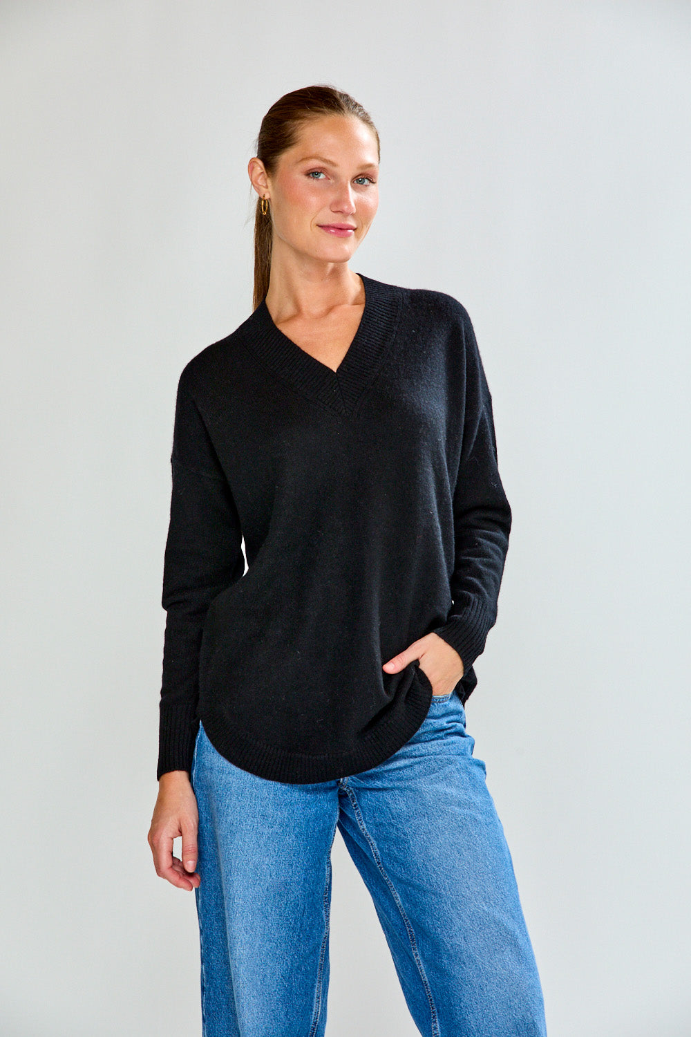 Woman wearing a black sweater and blue jeans against a plain background