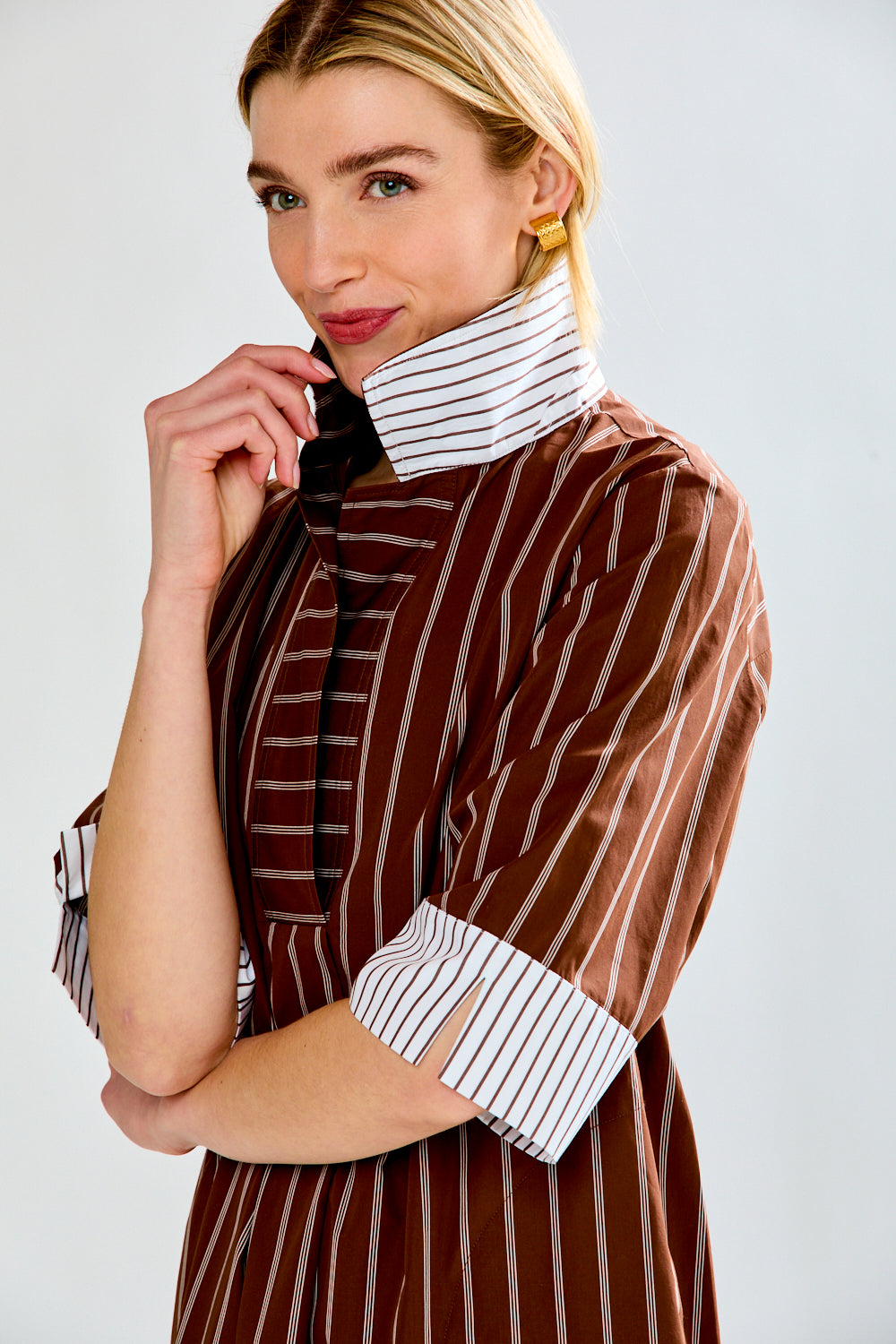 Woman wearing a brown pinstripe dress with a white collar against a plain background