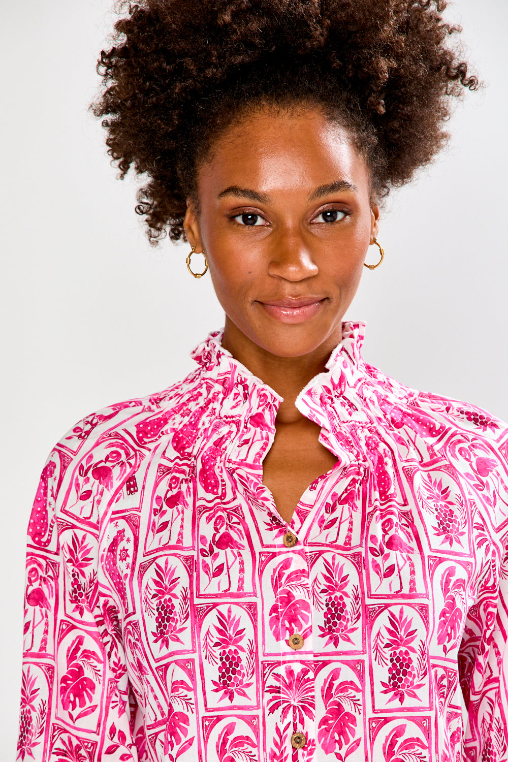 Woman wearing a pink patterned blouse and pink pants on a white background