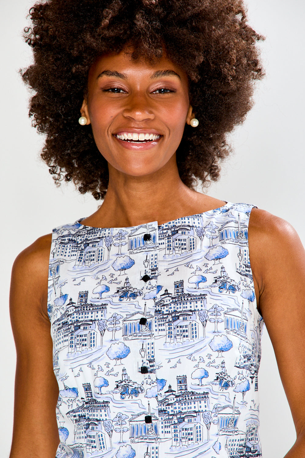 Woman wearing a patterned top and white pants against a plain background