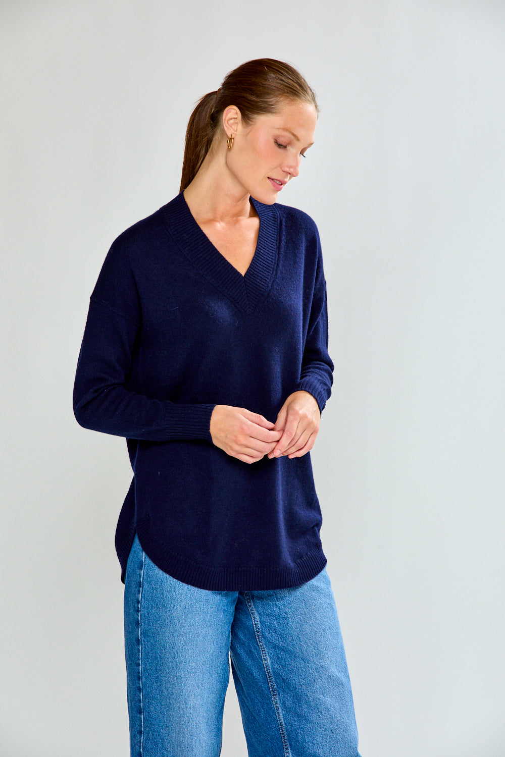 Woman wearing a navy sweater and blue jeans against a plain background