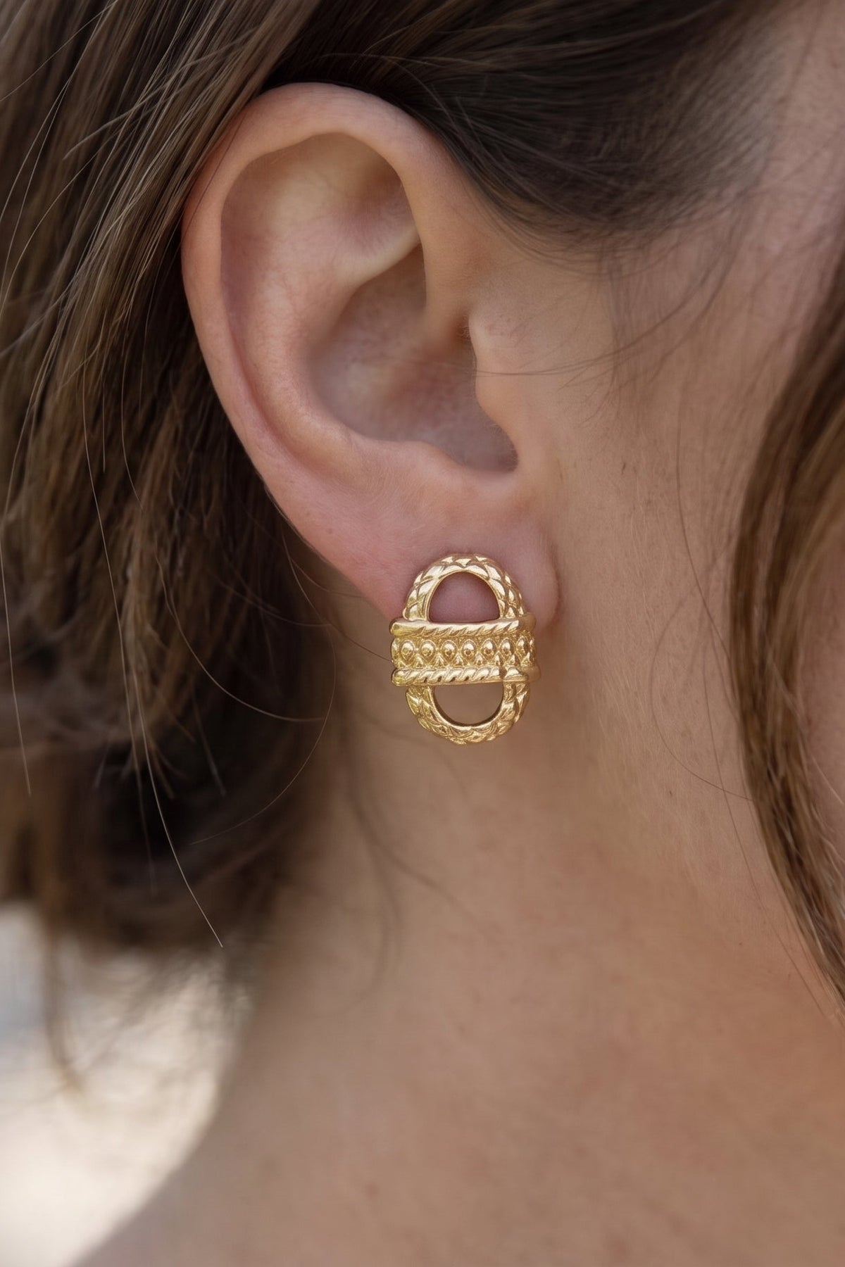 A close-up of a woman's ear wearing a textured gold hoop earring.