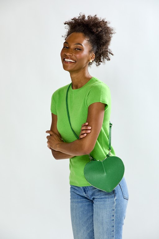 Woman wearing a green shirt and blue jeans, holding a green handbag against a white background