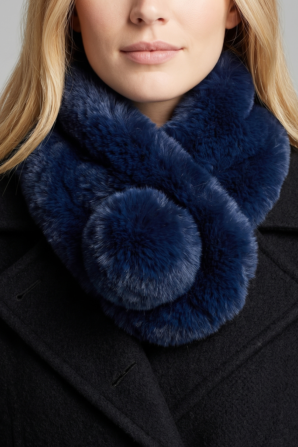 A close-up of a model wearing a thick, luxurious navy blue faux fur scarf with a matching pom-pom detail, styled with a black coat.