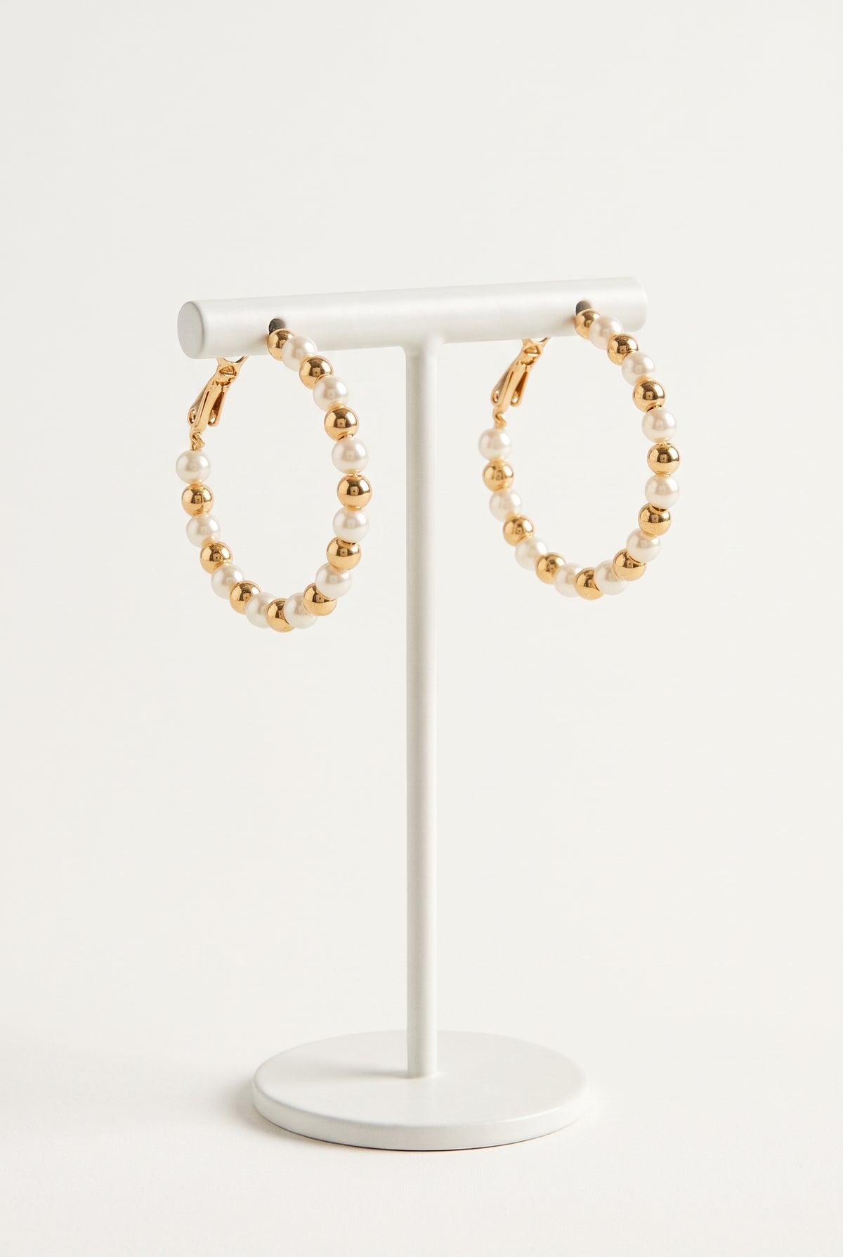Gold and white pearl hoop earrings displayed on a white stand against a clean white background.