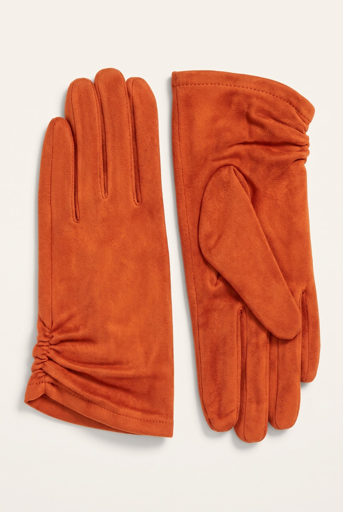 A pair of rust-orange suede gloves, one showing the back of the hand and the other showing the palm side, laid flat on a light cream background.