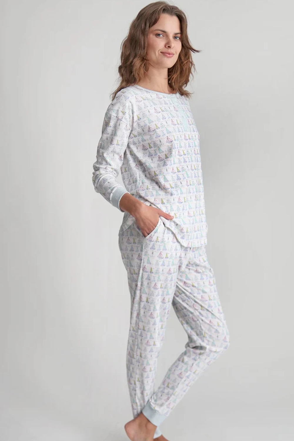 The Holiday Sailboat Long Pajama Set in white with a colorful sailboat print long sleeve top and matching pants modeled by a woman barefoot indoors