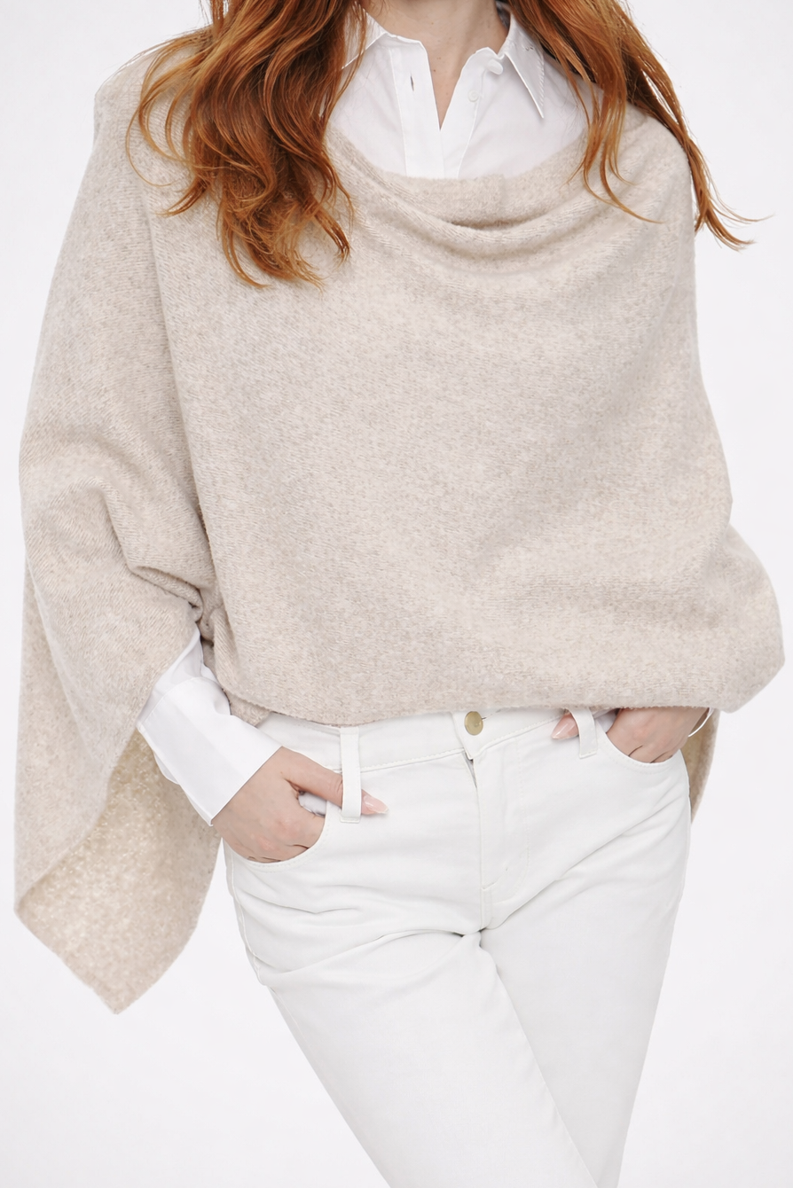 Woman wearing a beige sweater over a white shirt with white pants on a white background
