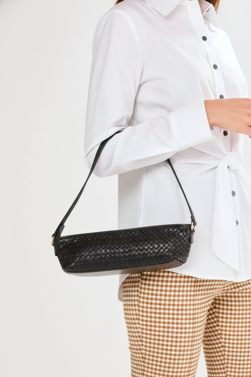 Person wearing a white shirt and brown checkered pants with a black woven handbag on a light gray background
