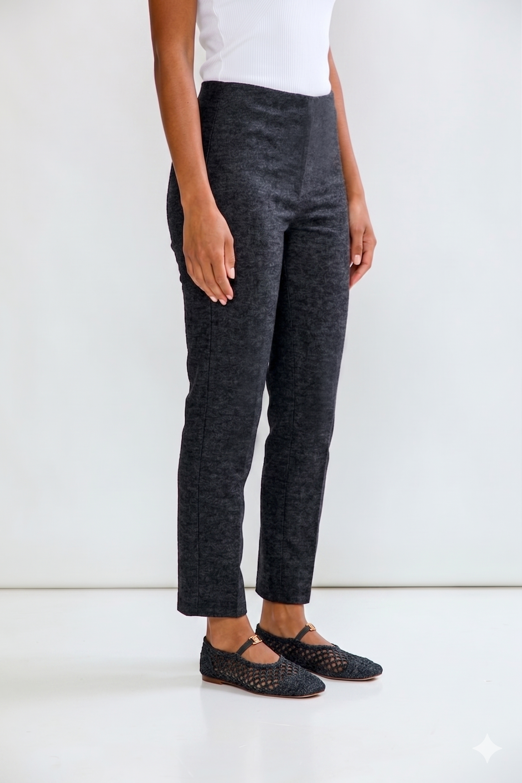 Person wearing dark gray pants and black shoes on a white background