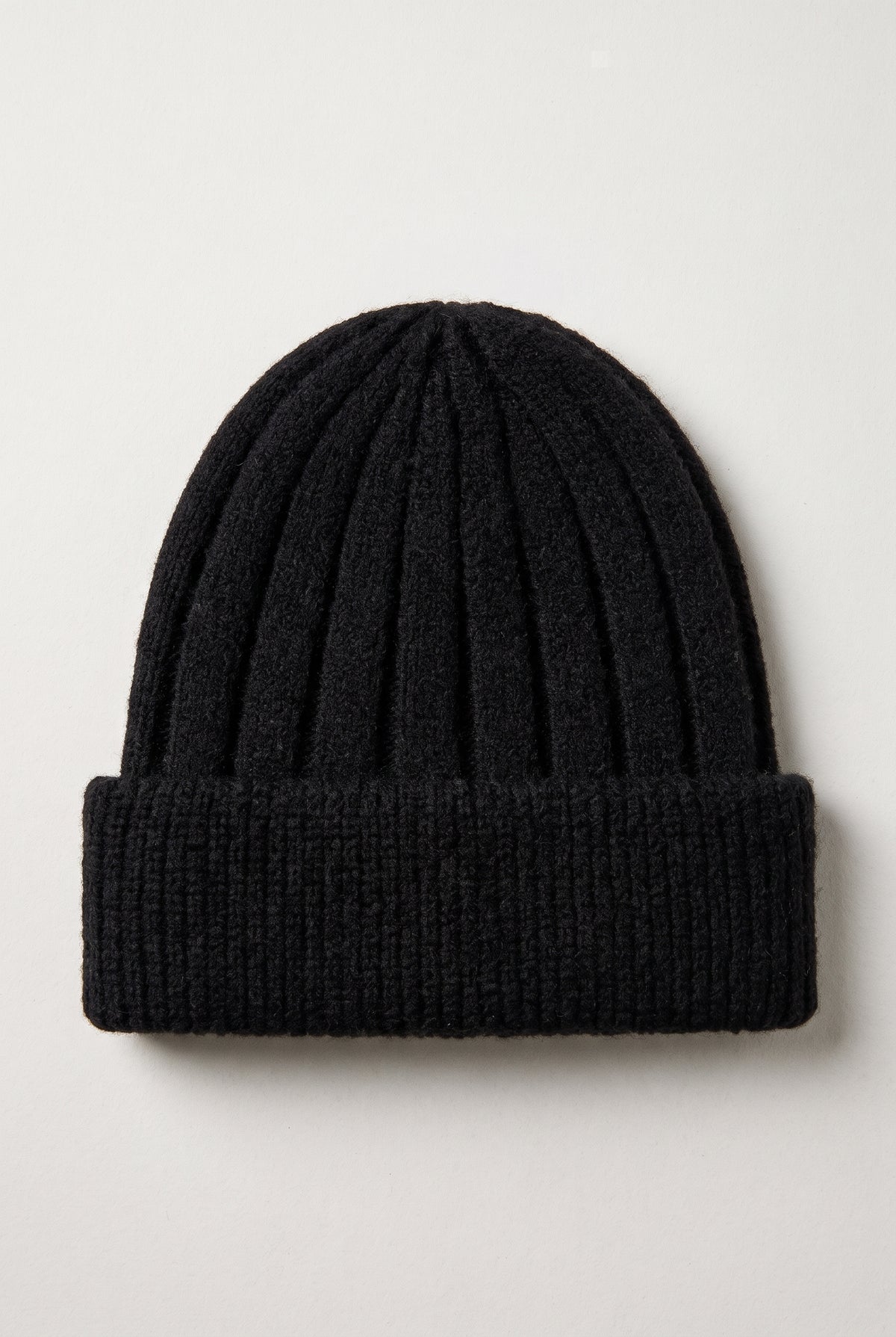A black ribbed knit beanie hat with a folded cuff, photographed flat against a light gray background.